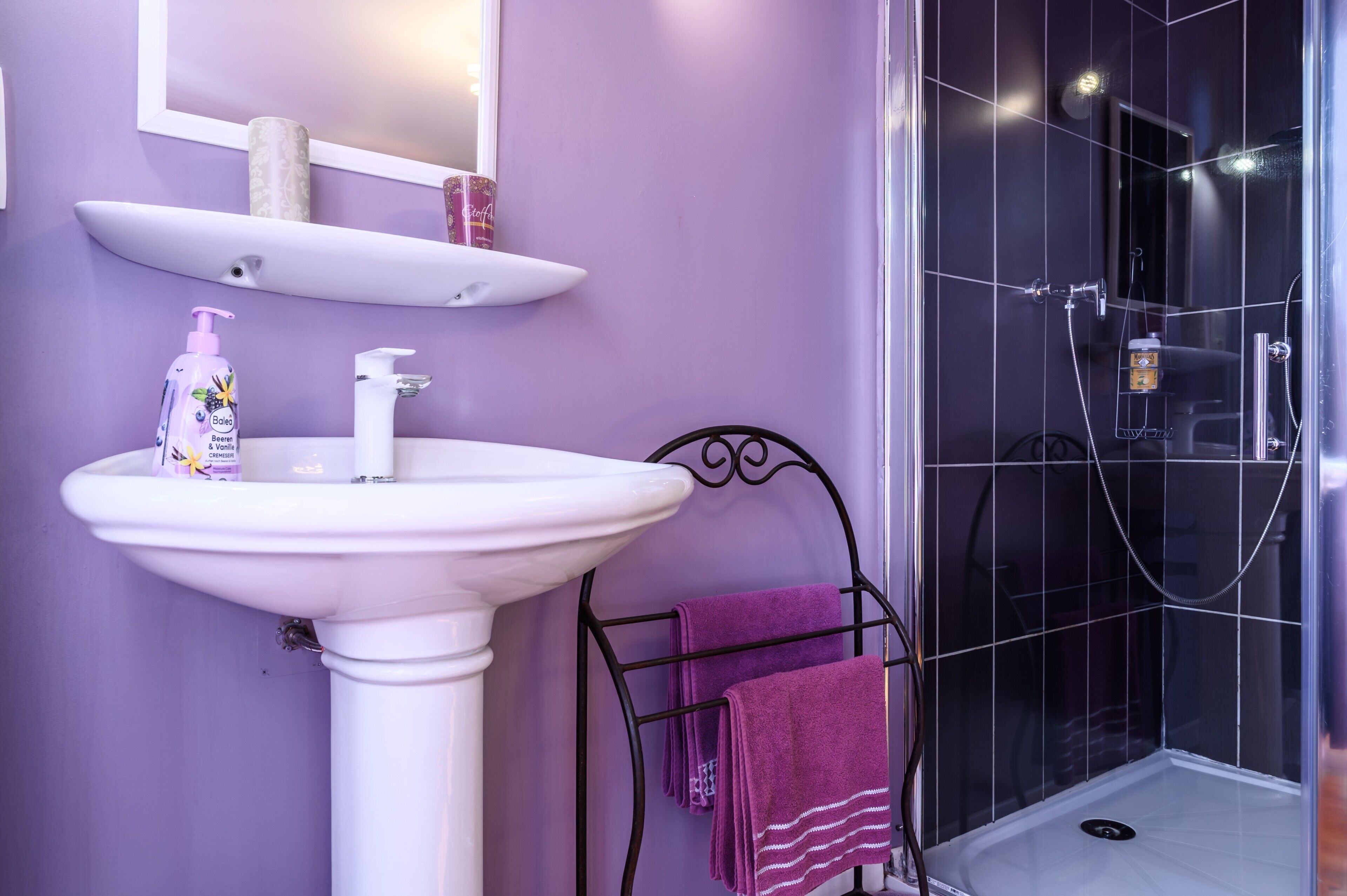 Ein Badezimmer mit einem weißen Waschbecken, einem Spiegel, einer Ablage mit Toilettenartikeln und einer Duschkabine.