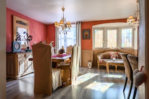 Ein Essbereich mit Tisch, Stühlen, einer Chandelüster und einem Fenster mit Vorhängen.