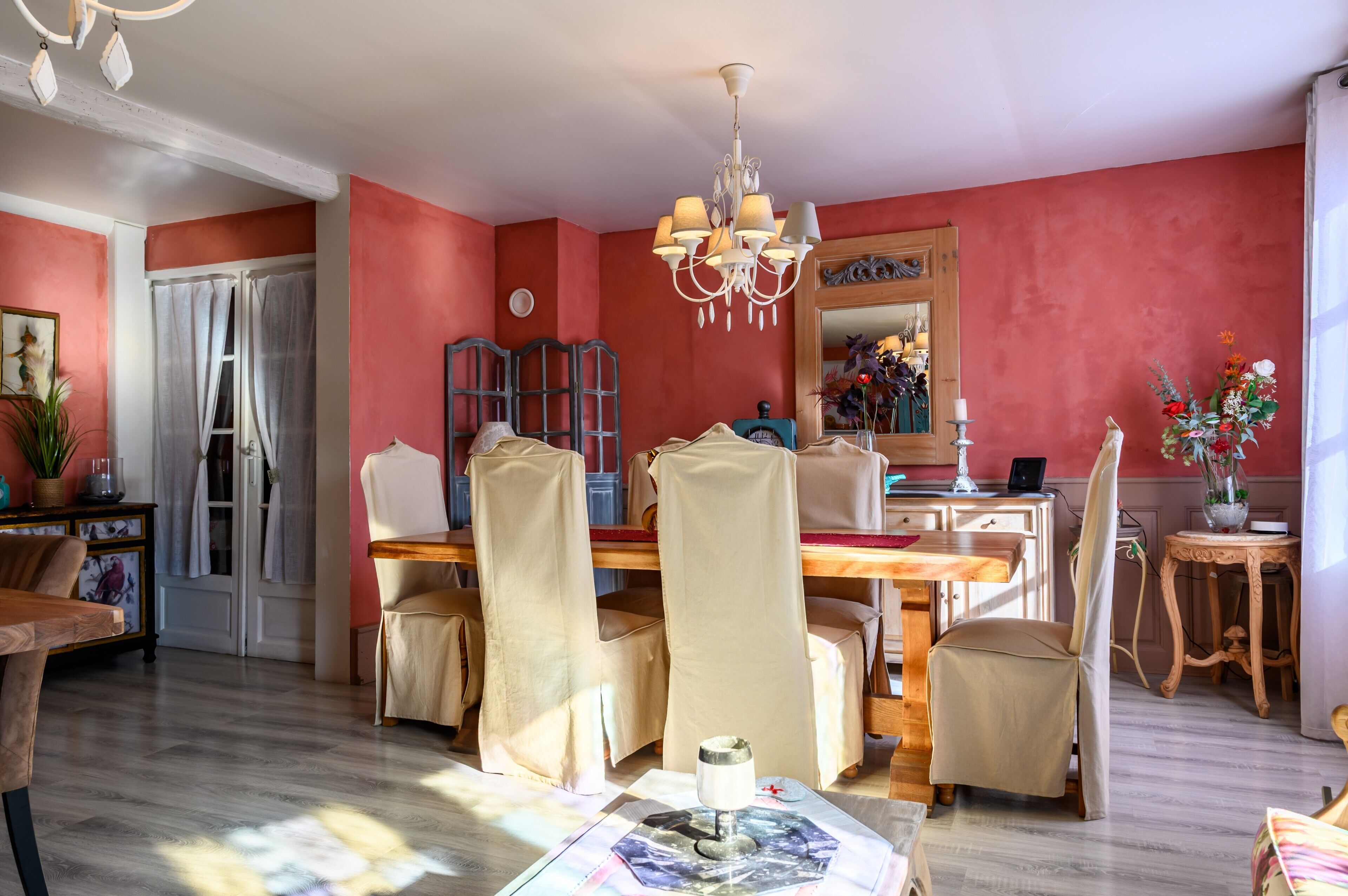 Un coin repas avec une table en bois, des chaises de couleur beige, un lustre et un miroir au-dessus de la table.