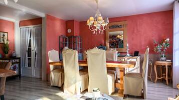 Un coin repas avec une table en bois, des chaises de couleur beige, un lustre et un miroir au-dessus de la table.