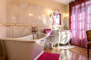Un baño con una bañera tipo pata de león, un tocador blanco, un espejo y una silla.
