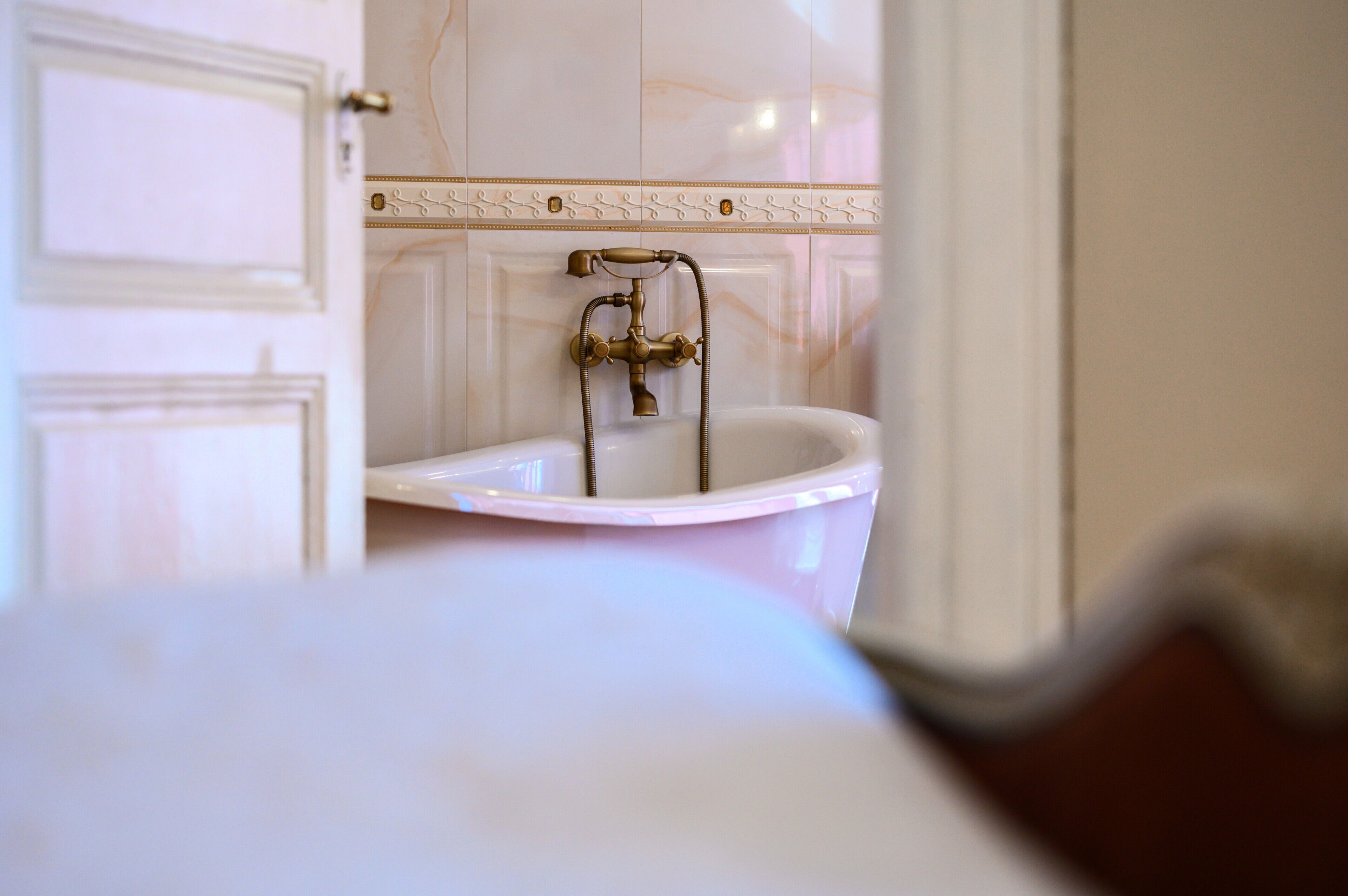 A bathroom with a white bathtub, a brass faucet, and a tiled wall.