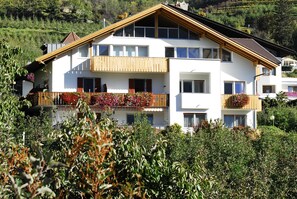 Ein zweistöckiges Gebäude mit Balkonen, großen Fenstern und hügeliger Landschaft im Hintergrund.