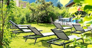 Ein Poolbereich mit Liegestühlen und einem Tisch, umgeben von Grünflächen und Blick auf die Berge.