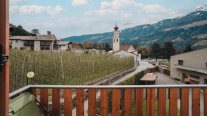 Ein Balkon mit Blick auf einen Weinberg, einen Kirchturm und ein Gebirge.