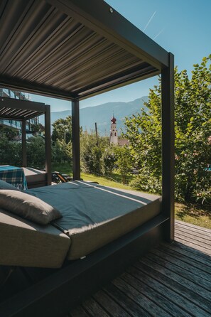 A bed in a covered outdoor area with a view of a church and mountains. - Room 'Garni Unterweggütl Fußballzimmer' with Mountain View, Shared Pool and Wi-Fi (Naturno)