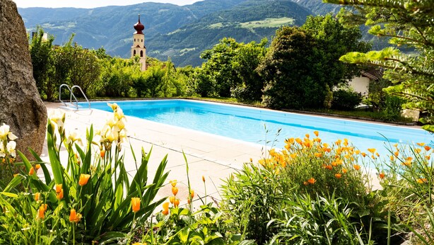 Ein Schwimmbecken mit Blick auf Berge und ein Kirchturm.