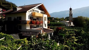Ein zweistöckiges Haus mit Balkon und Glockenturm, vor einer Berglandschaft.