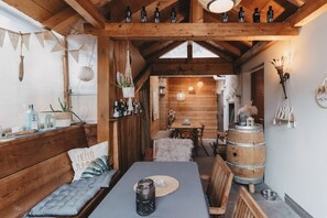 A cozy wooden interior with a dining area, wooden beams, and a bar area with bottles.
