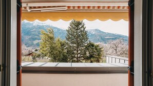 A balcony with a view of snow-capped mountains, a pine tree, and a building in the background. - Apartment 'Jack Daniels' with Mountain View, Shared Pool and Wi-Fi (Naturno)