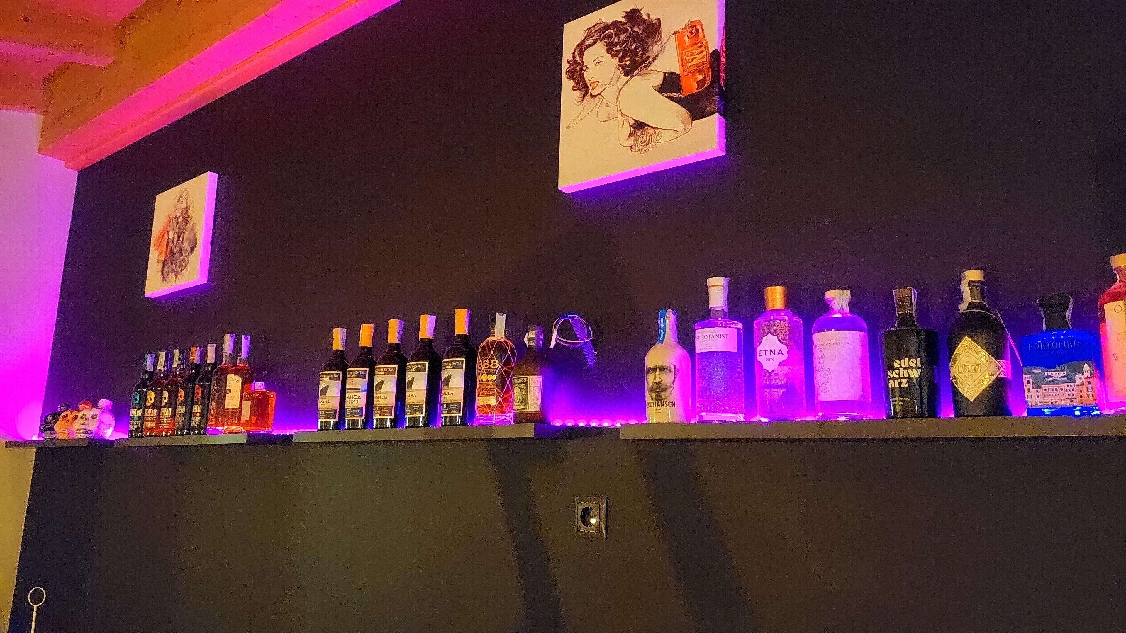 Eine Bar mit verschiedenen Spirituosenflaschen und zwei gerahmten Bildern an der Wand.