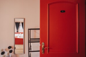 Une porte rouge avec une plaque portant un numéro, un miroir et un présentoir en métal noir avec des paniers blancs.