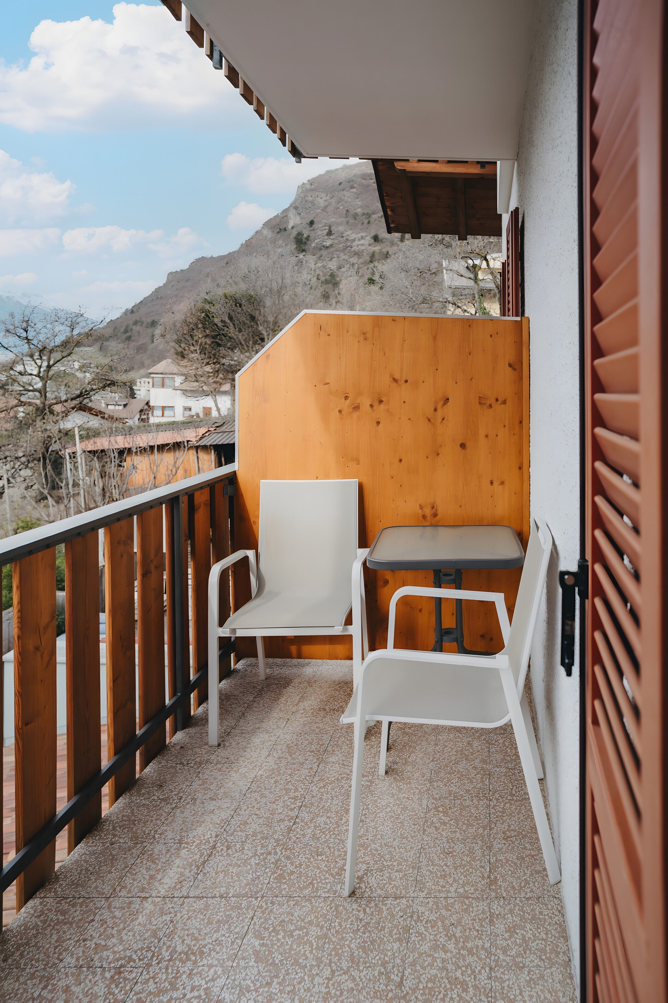 Ein Balkon mit einer Holzwand, zwei weißen Stühlen und einem Tisch.