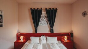 A bedroom with a bed, two bedside tables with lamps, a red headboard, and dark curtains. - Room 'Garni Unterweggütl Love' with Mountain View, Shared Pool and Wi-Fi (Naturno)