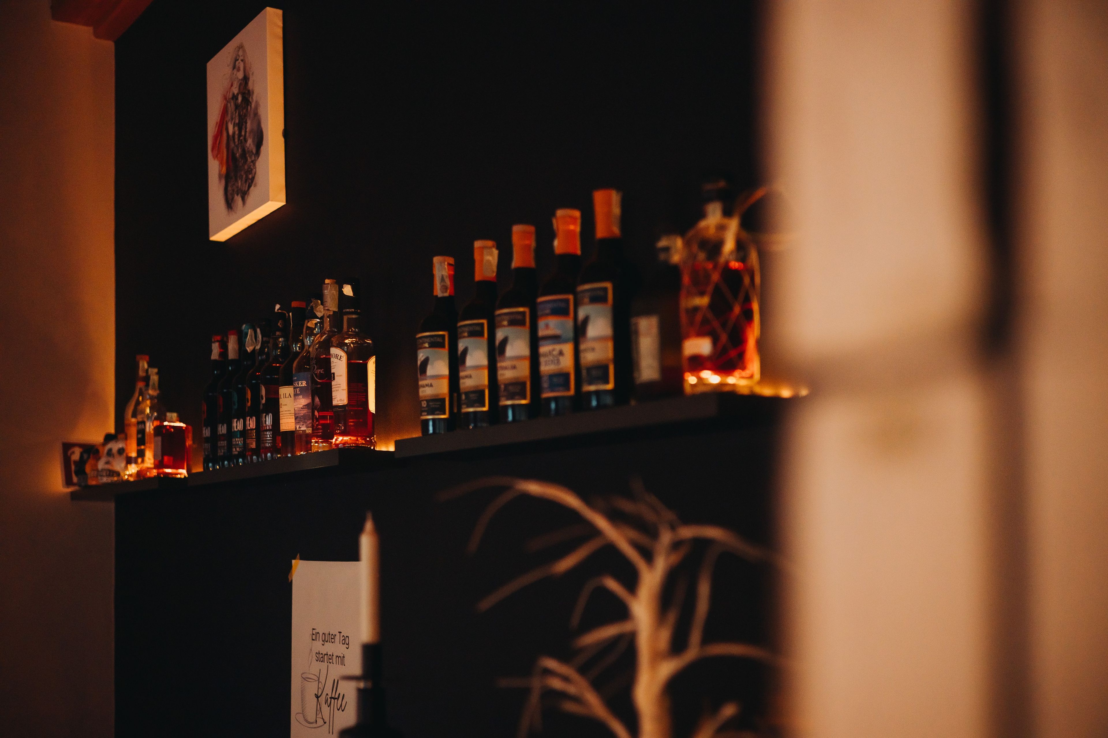 Zona de bar amb diverses ampolles d'alcohol i un cartell que diu 'Ein guter Tag startet mit Kaffee'.