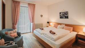 Ein Hotelzimmer mit Bett, Sessel, Nachttisch, Fenster mit Vorhängen und einem Wandbild.