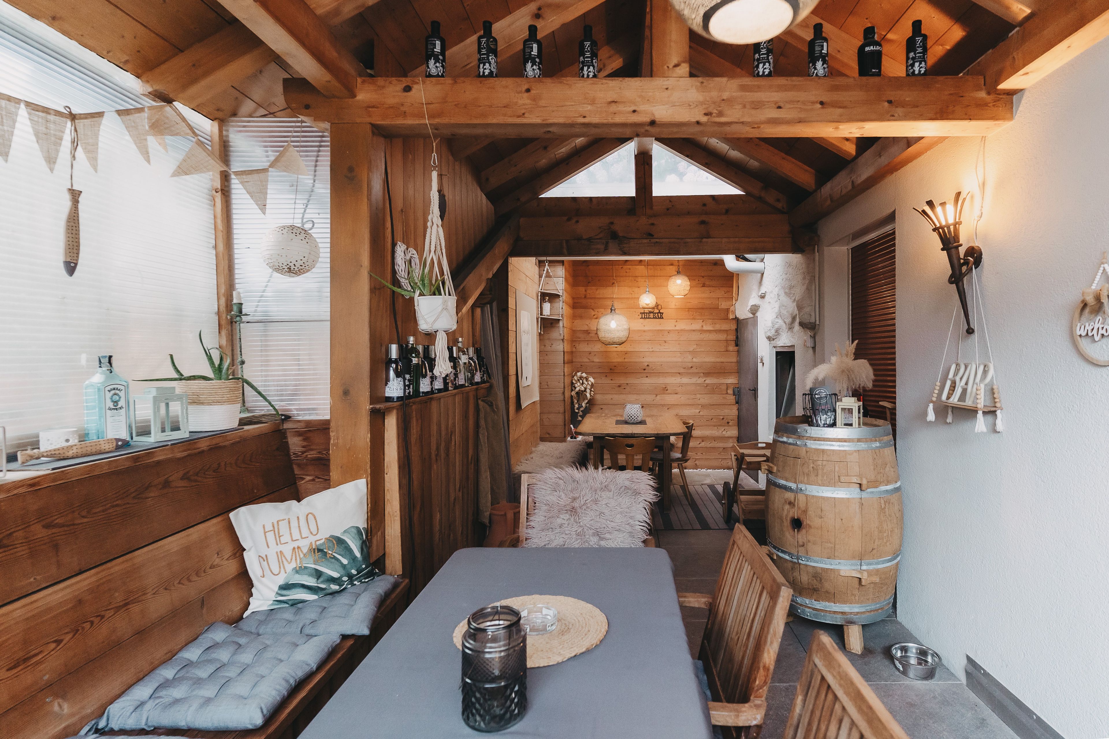 A cozy wooden interior with a dining area, wooden beams, and a bar area with bottles.