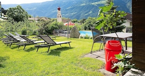 Ein grüner Außenbereich mit Liegestühlen, einem Tisch und einer roten Mülltonne.