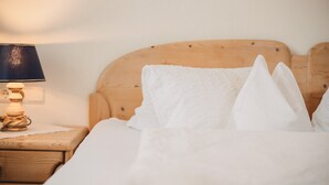 A neatly made bed with white linens and pillows, a wooden headboard, and a bedside lamp on a wooden nightstand. - Room 'Tiroler' with Mountain View, Shared Pool and Wi-Fi (Naturno)