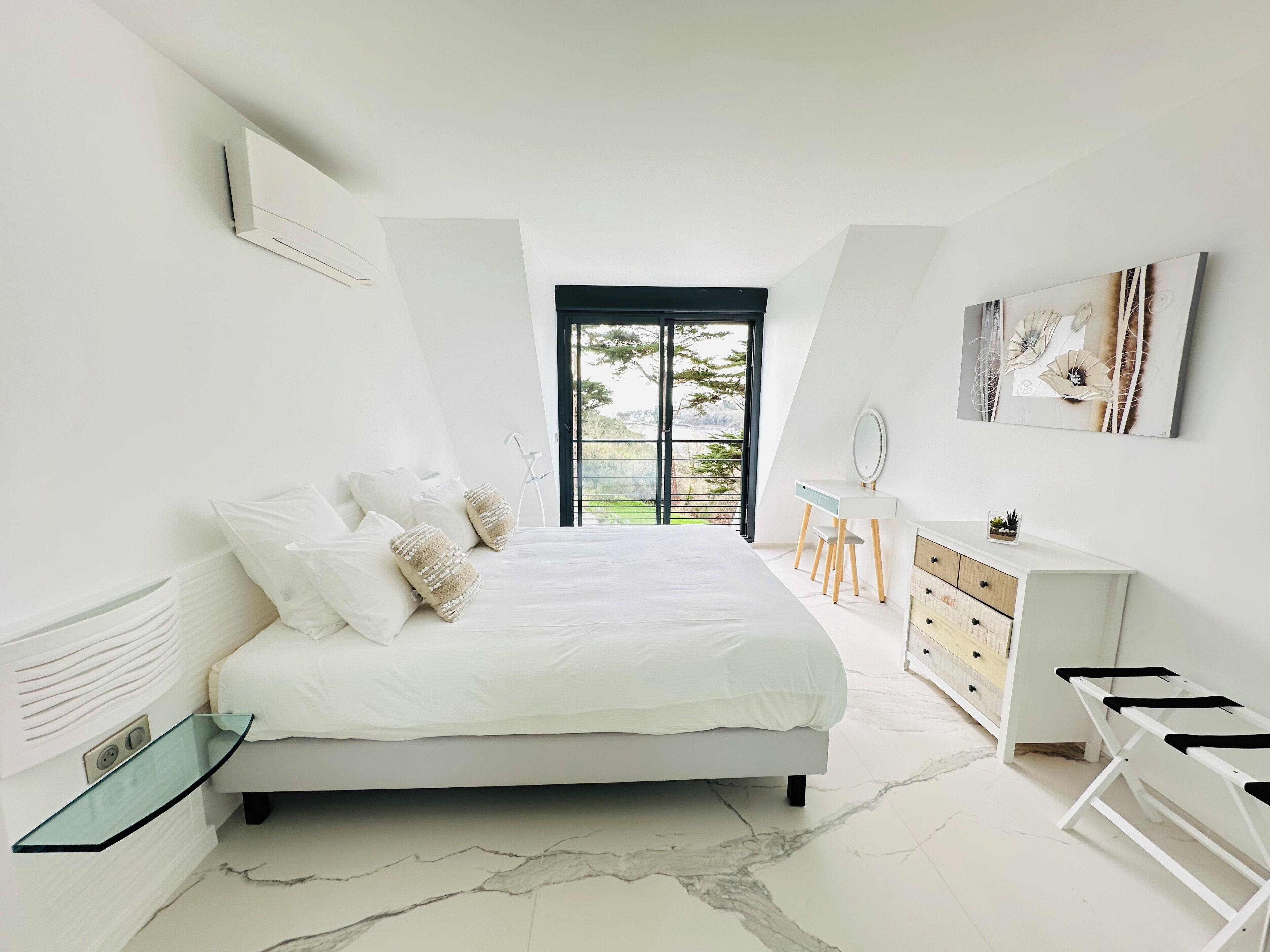 Un dormitorio con cama, escritorio, cómoda y vista al exterior.