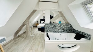 A modern bedroom with a sloped ceiling, a large bed, a bathtub, and a skylight. - Avocet - Laïta (Guidel)