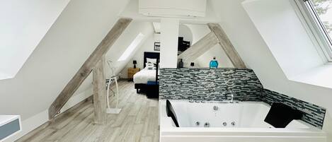 Un dormitorio moderno con techo inclinado, una cama grande, una bañera y un tragaluz.