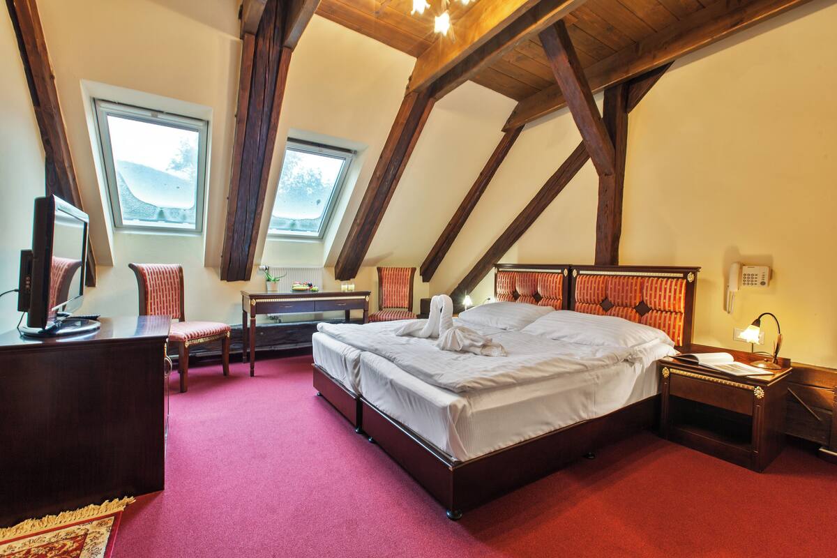 A bedroom with a large bed, a desk, a chair, a TV, and a telephone.