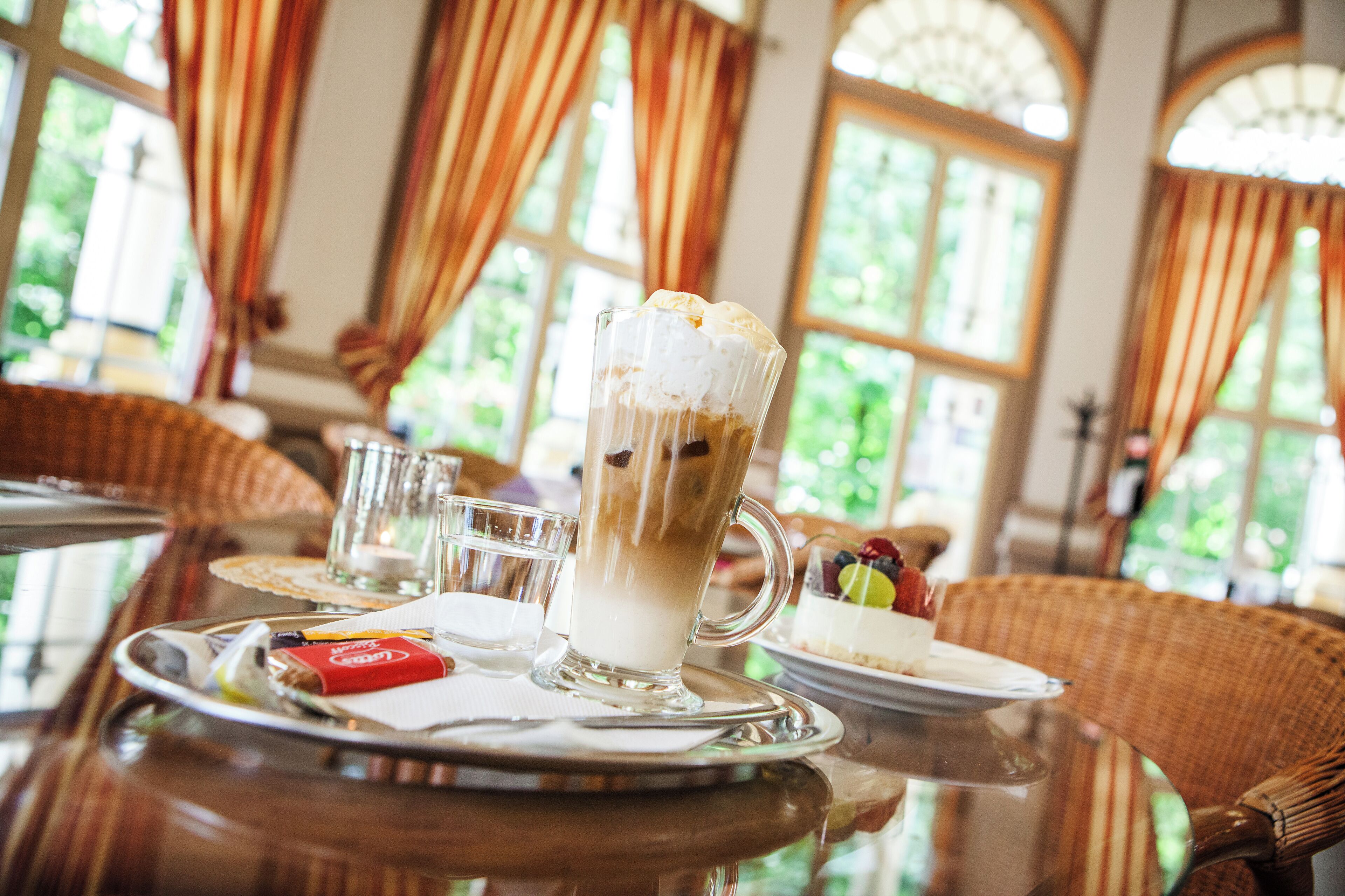 A dining table with a dessert, a glass of iced coffee, and a plate with a red item.