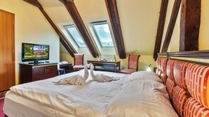 Habitación de hotel con una cama grande, televisión, escritorio con computadora y dos ventanas.