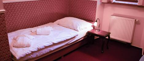A single bed with a wooden frame, a bedside table with a lamp, and a radiator on the wall.
