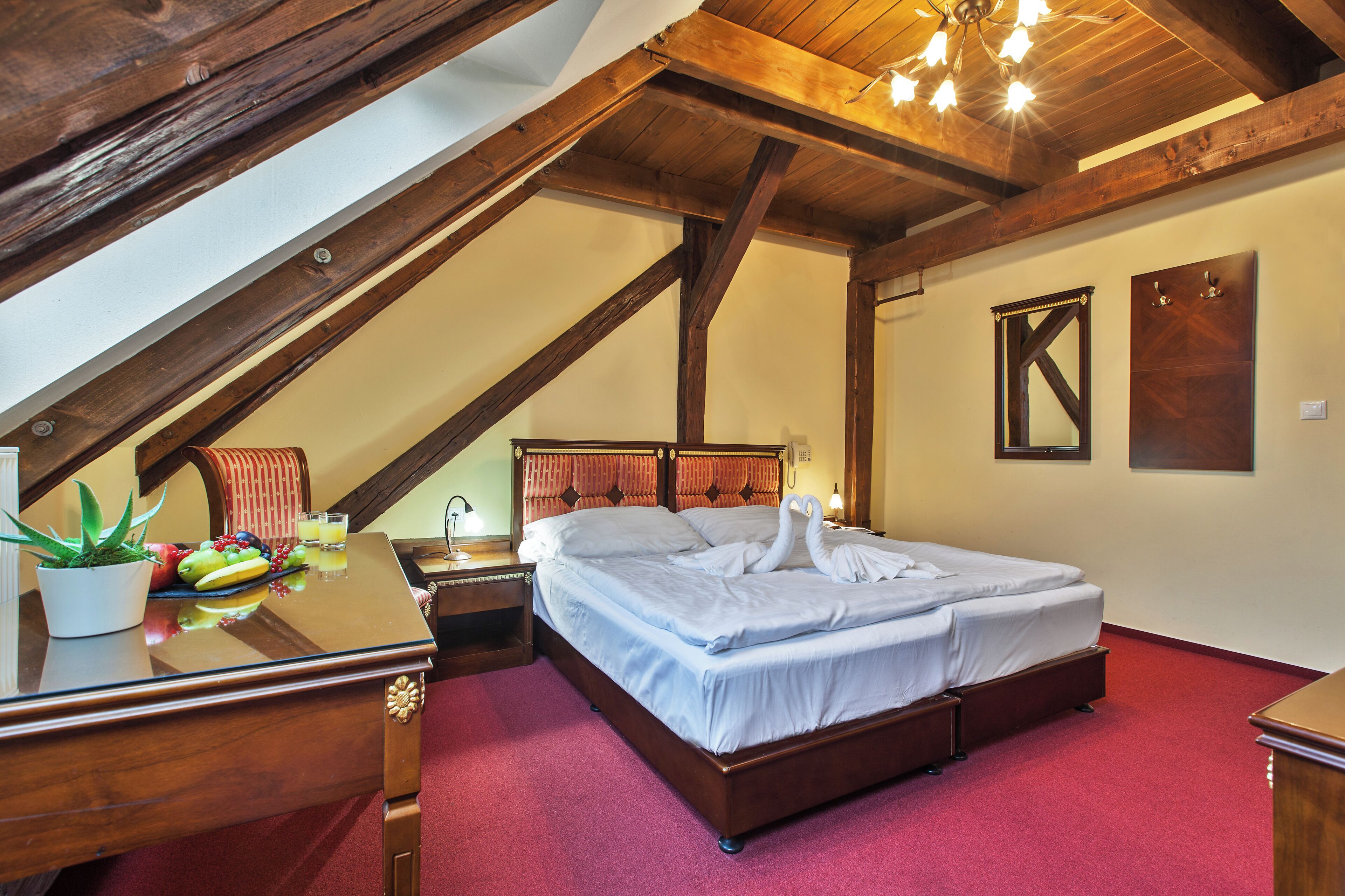 Une chambre avec un plafond en bois, un lit recouvert de draps blancs, une table de chevet, une petite table à côté du lit avec des fruits et une plante en pot.