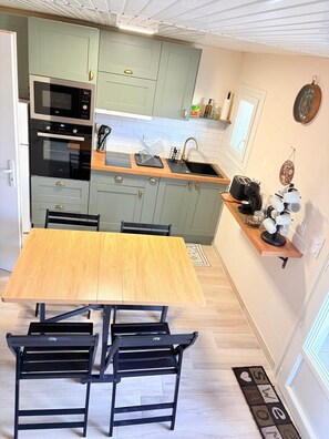 Uma cozinha compacta com uma mesa de jantar, cadeiras, micro-ondas, forno e pia.