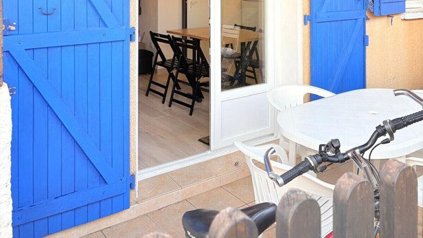 Eine überdachte Terrasse mit blauen Fensterläden, ein Essbereich mit Tisch und Stühlen sowie ein Fahrradständer.