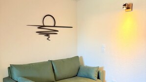 Ein Zimmer mit einem grünen Sofa, einem Holztisch und einer Wandleuchte.