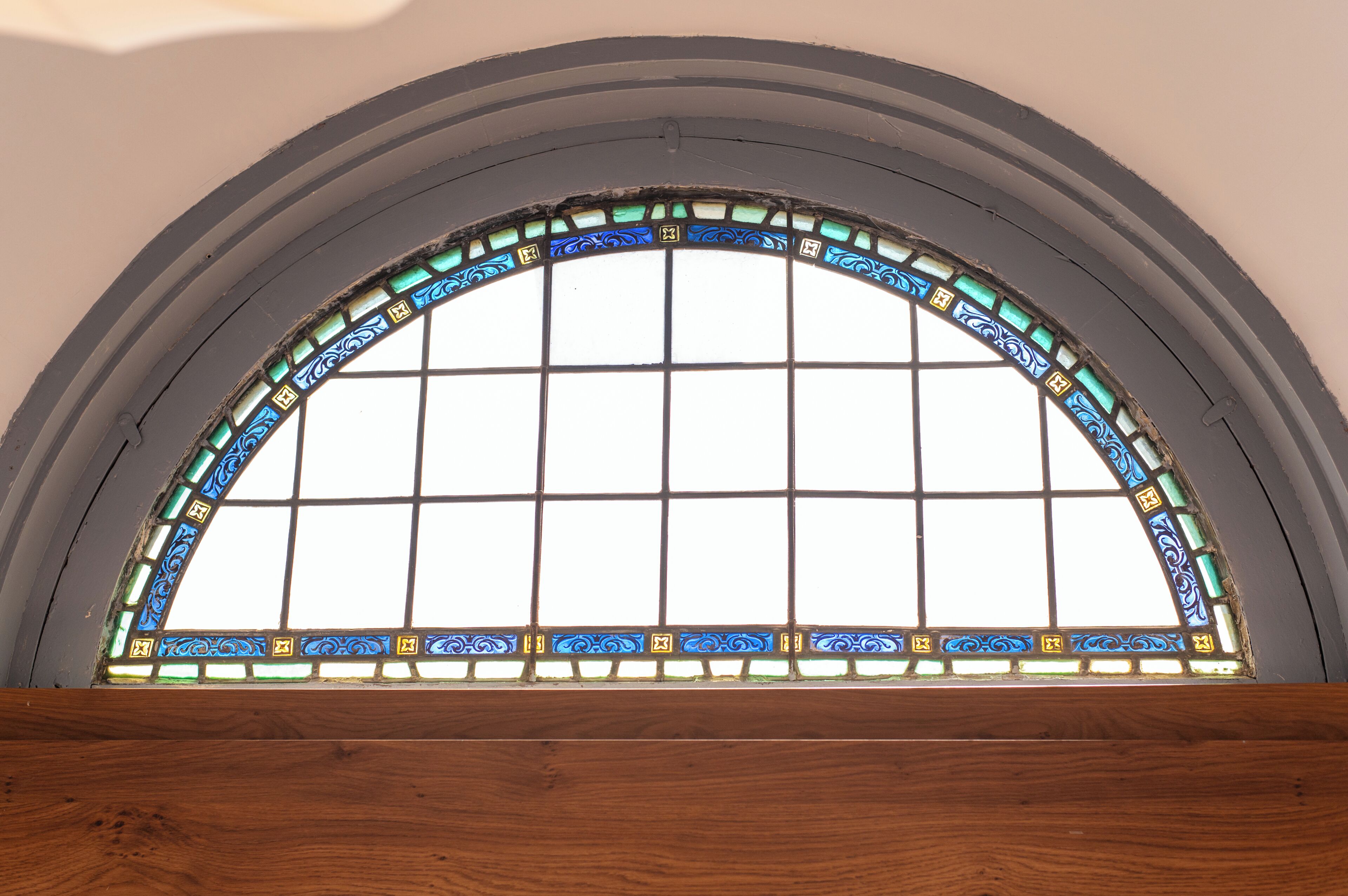 A large arched window with a grid pattern and decorative stained glass.