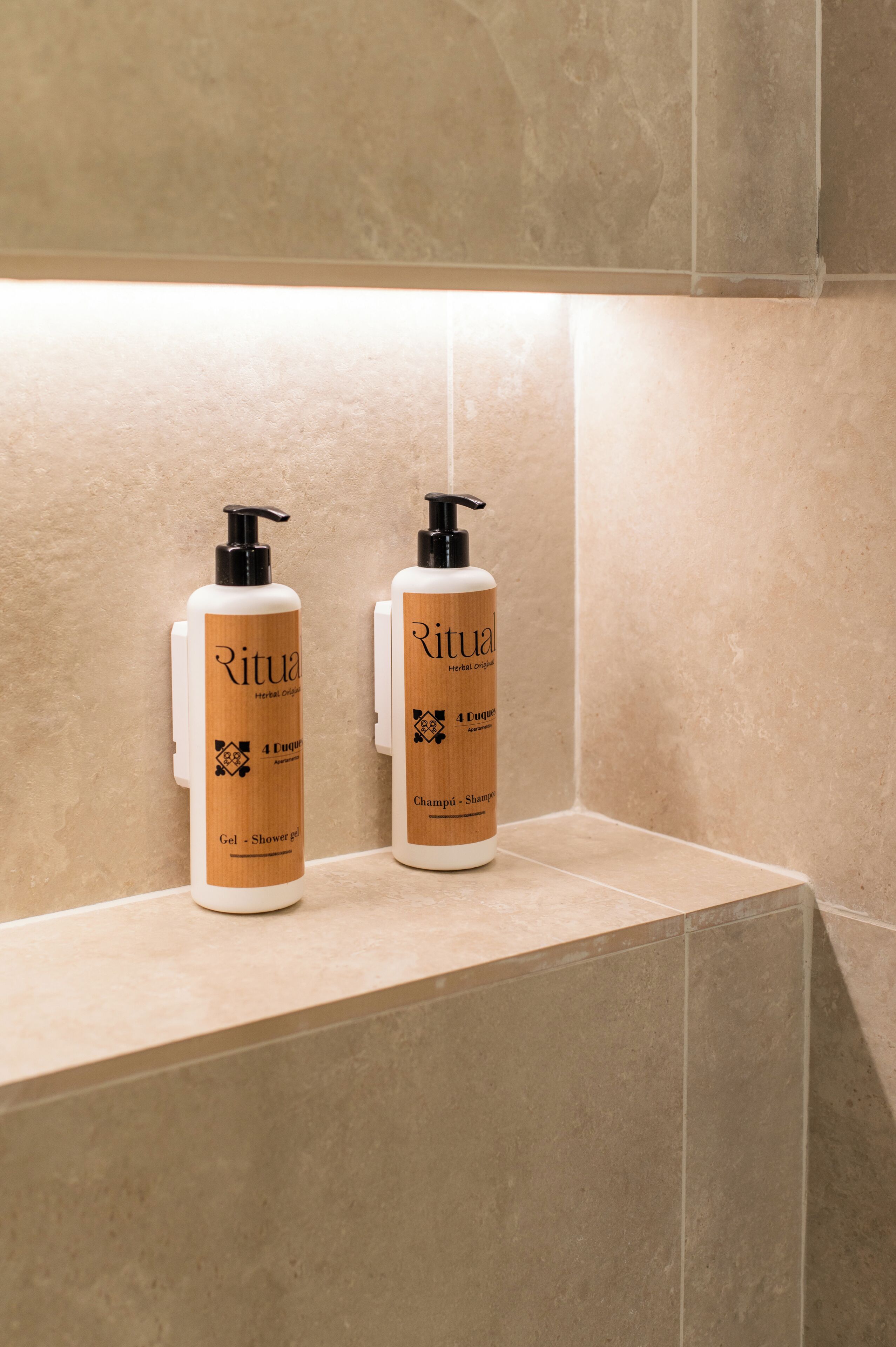 Duas embalagens de shampoo e condicionador herbal orgânico Ritual sobre um balcão revestido com azulejos bege.