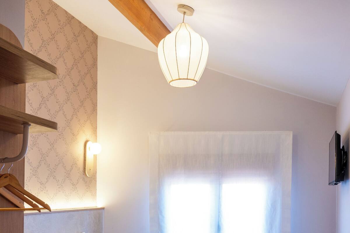 Ein Schlafzimmer mit einem Bett, einer Hängelampe, einem Fenster mit Vorhängen und einem Holzboden.