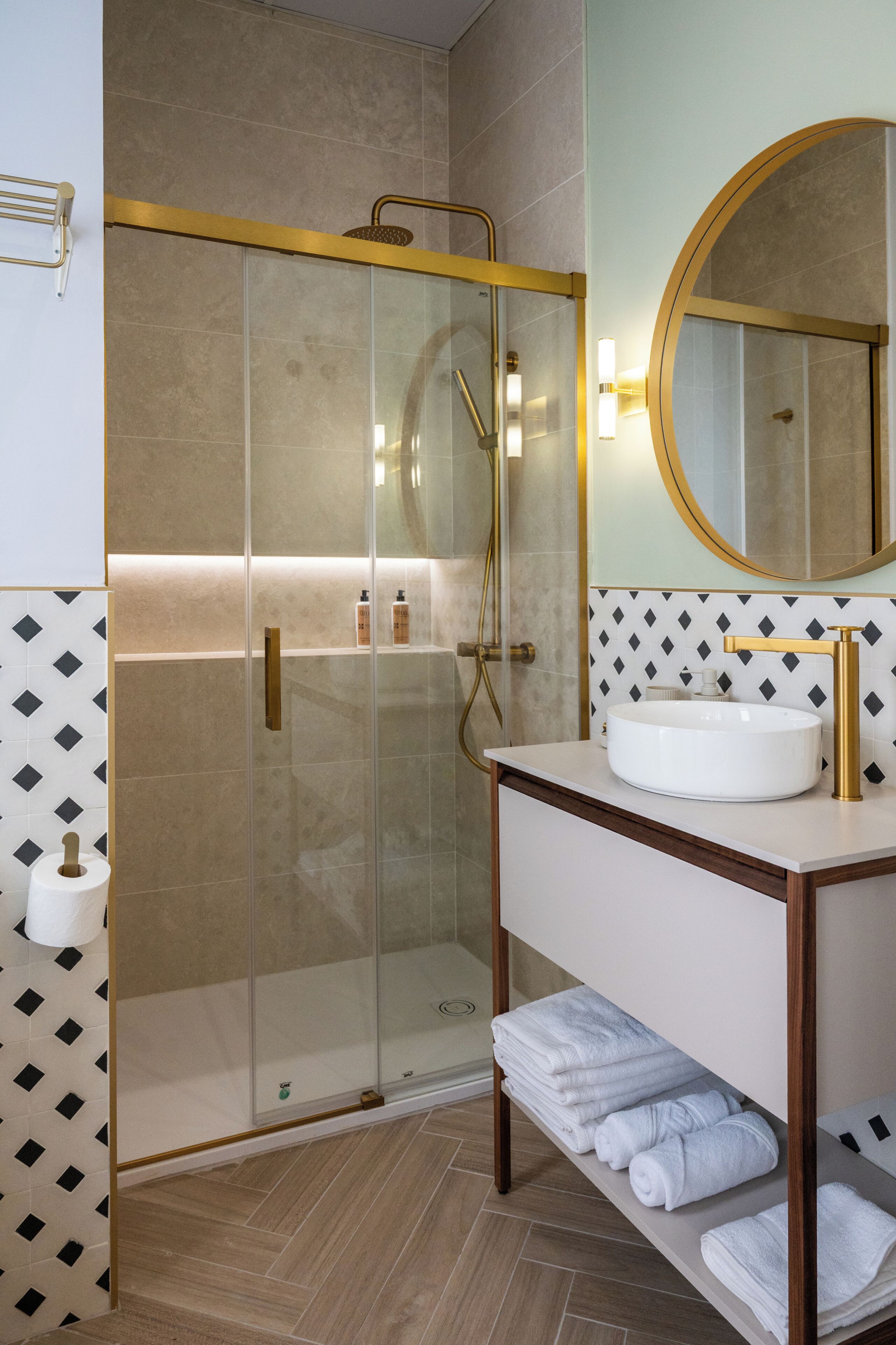Une salle de bain moderne avec une douche à parois de verre, un lavabo blanc et un miroir avec un cadre doré.