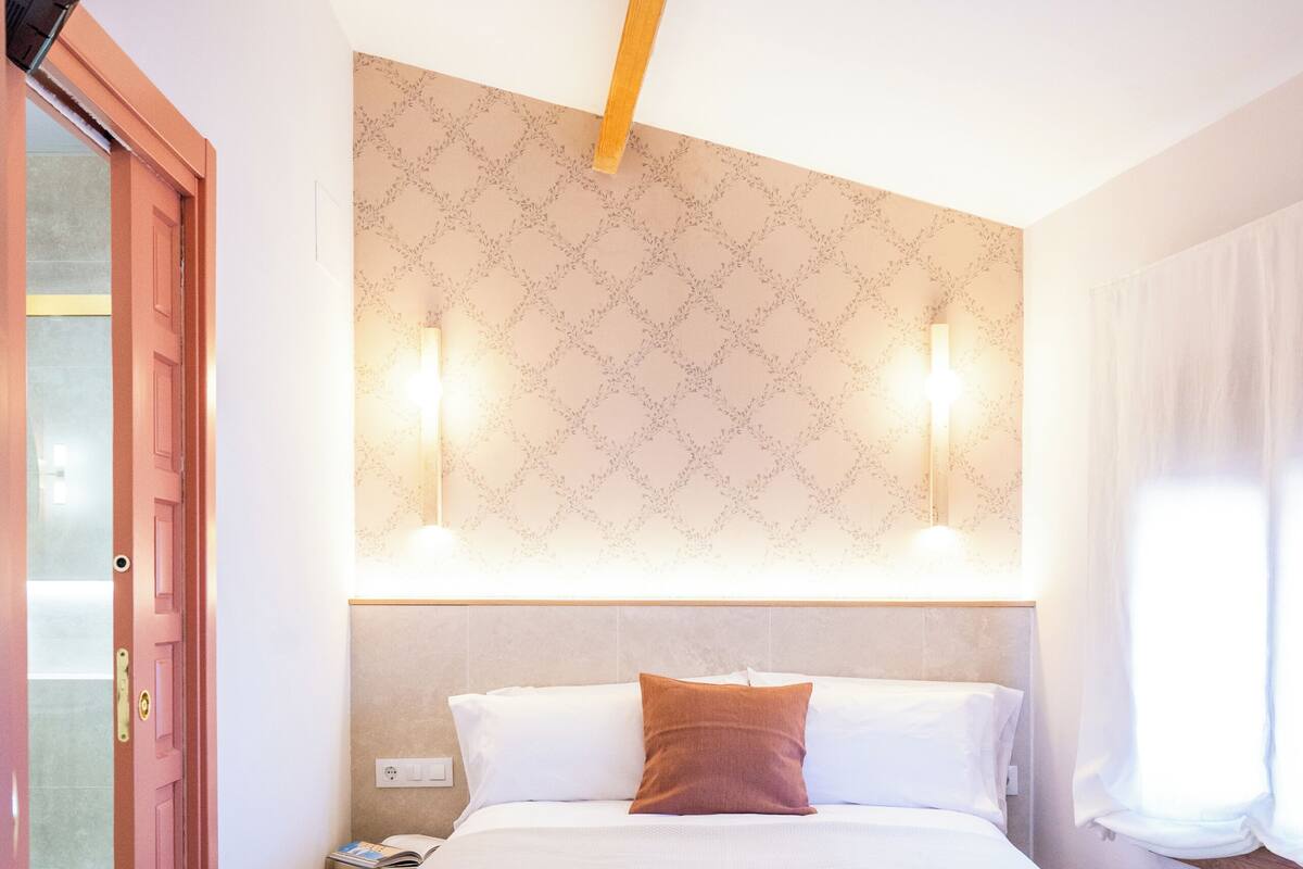 Ein Hotelzimmer mit einem Bett, einem Nachttisch, einer Wandleuchte und einer Tür.