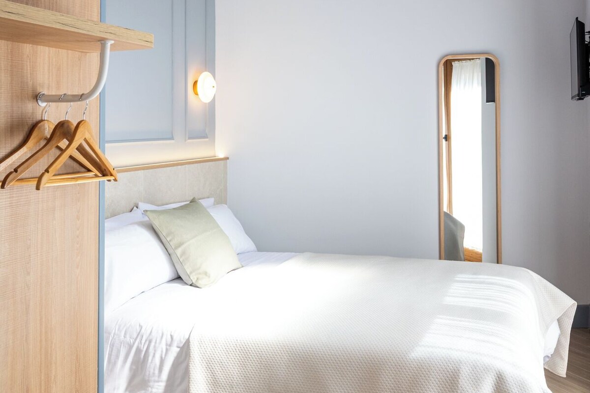 A bedroom with a bed, wooden furniture, a hanging light fixture, and a mirror.