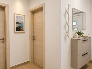 Ein Flur mit zwei Holztüren, einem gerahmten Bild an der Wand, einem Spiegel und einem Schrank mit Pflanze und Schüssel darauf.