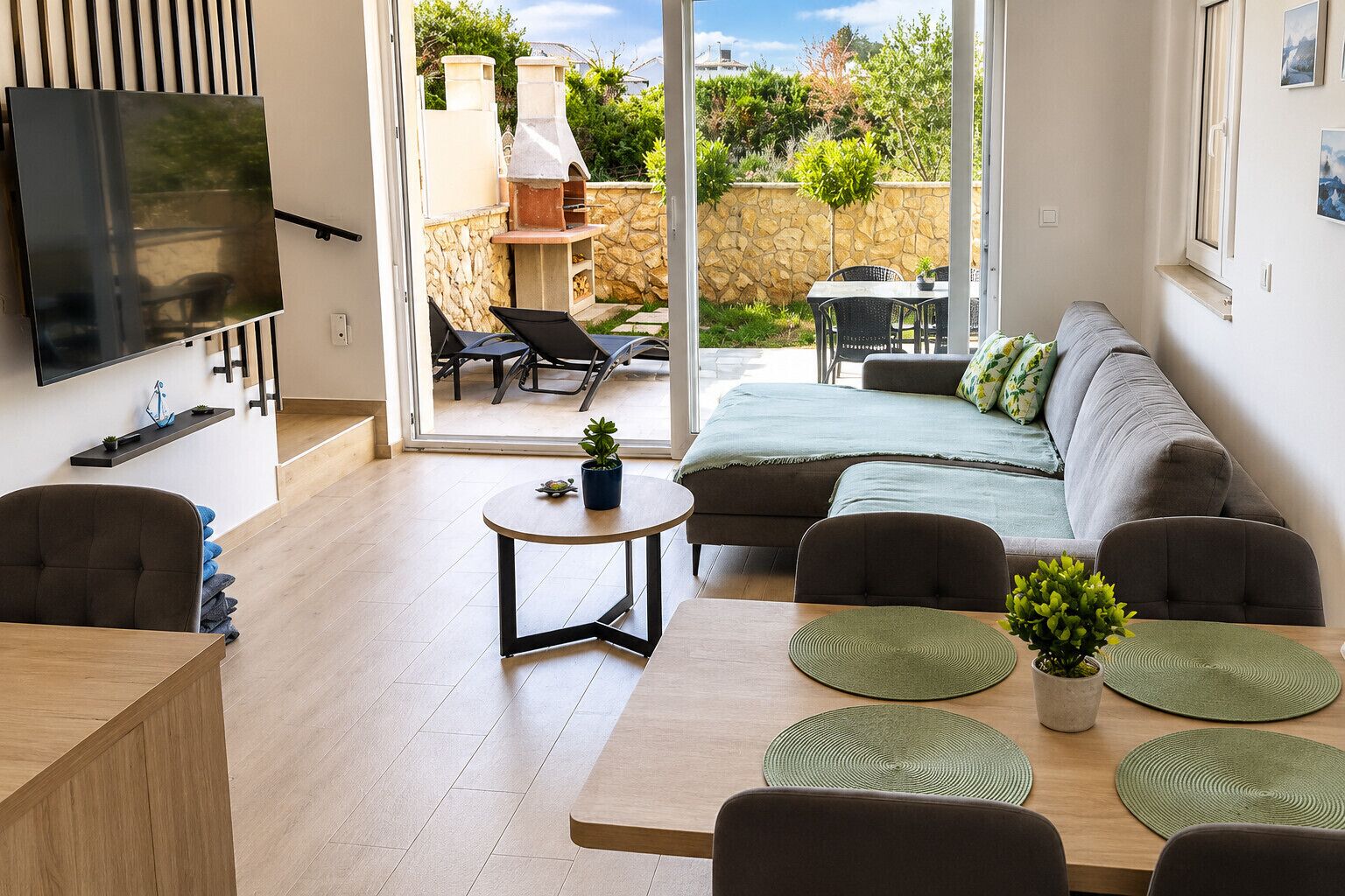 Een moderne woonkamer met een bank, stoelen, een televisie en een eethoek met een tafel en stoelen.
