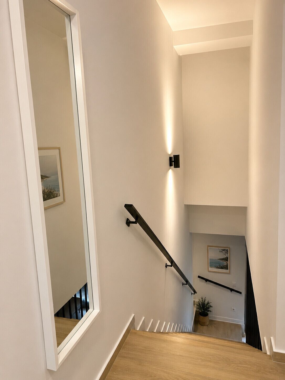Un intérieur moderne avec un escalier en bois, un tableau encadré au mur et un luminaire.
