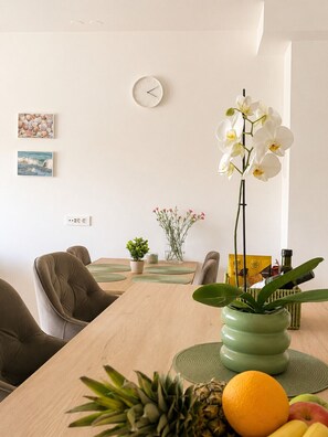 Uma sala de jantar com mesa de madeira, cadeiras, um relógio e objetos decorativos, incluindo flores e uma abacaxi.
