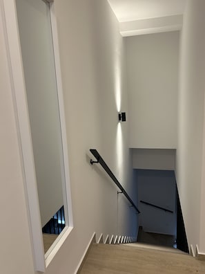Eine Treppe mit Handlauf, einer Wandleuchte und einem Fenster am oberen Ende.