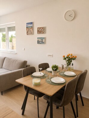 A dining area with a wooden table set for four, surrounded by chairs. There are wall-mounted artworks above the table and a wall clock to the right. - Apartment Mariner 1 with heated pool (Zaton)