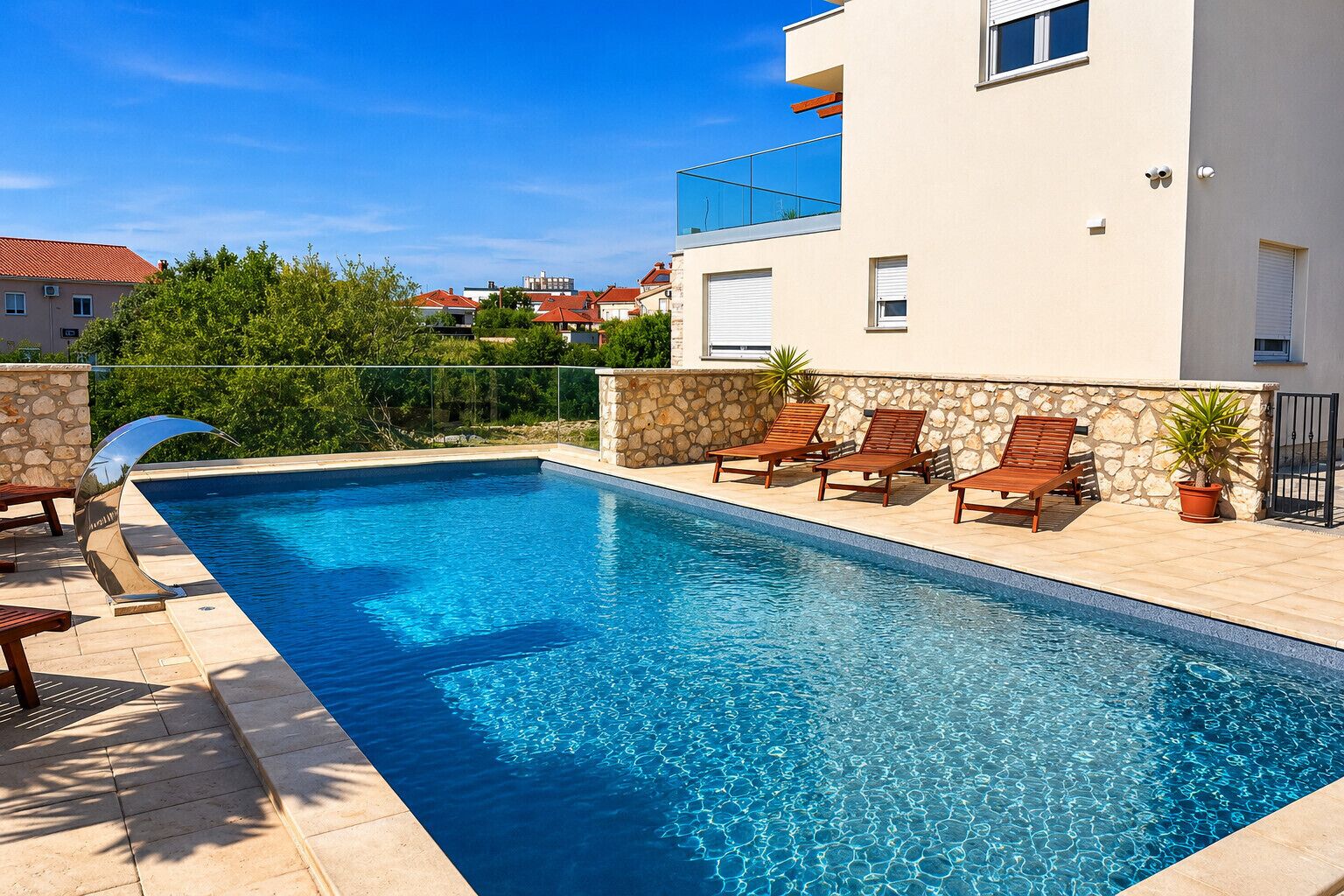 Une piscine rectangulaire avec un mur en pierre et un bâtiment moderne en arrière-plan.