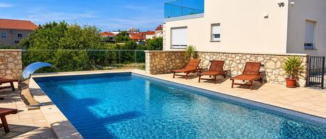 Une piscine rectangulaire avec un mur en pierre et un bâtiment moderne en arrière-plan.
