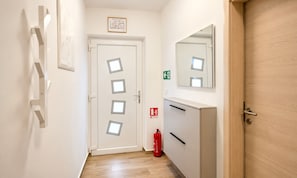 Ein Korridor mit einer weißen Tür, einem Feuerlöscher und einem Spiegel an der Wand.