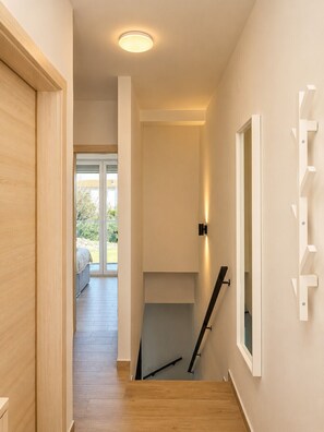 Ein Flur mit Holzboden, einer Treppe und einer Tür zu einem Zimmer mit einem Bett.
